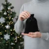 Main présentant un petit pochon en velours noir devant un sapin de Noël.