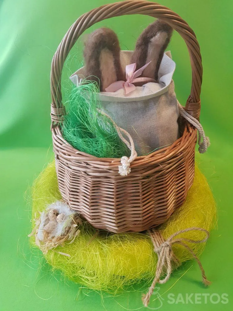 Petit panier avec un sac en lin dont dépassent les oreilles d’un lapin feutré en laine peignée.
