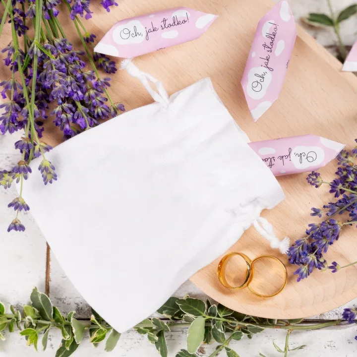 Pochon en satin blanc raffiné à côté d'alliances dorées et de fleurs.